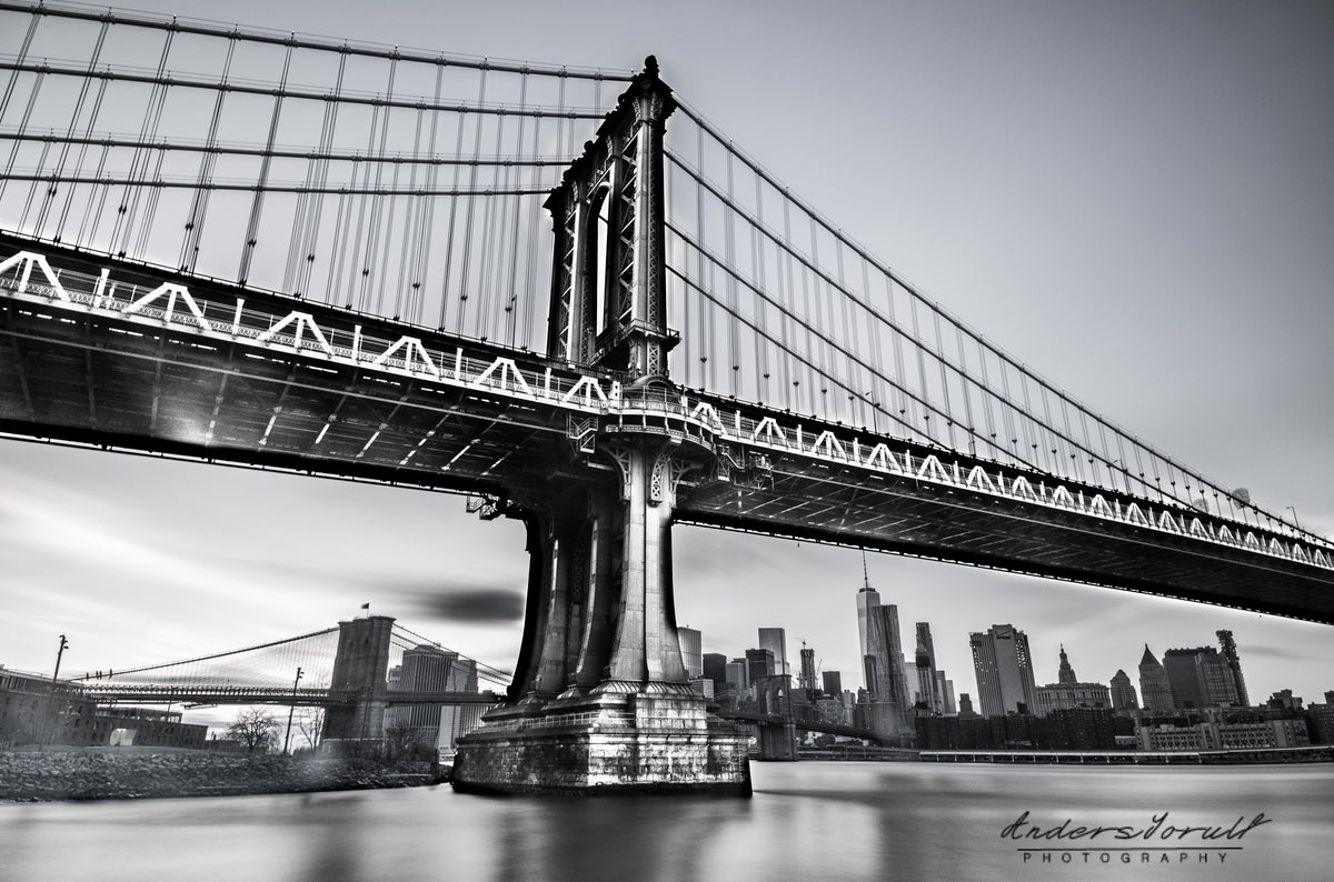 Black-and-white Manhattan Bridge spanning the East River, with New York buildings beyond. Photograph by Anders Jorulf.