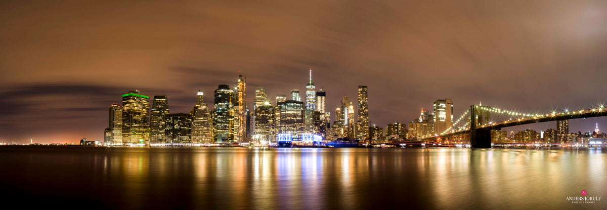 A wide panorama of illuminated Manhattan reflected in dark water. Photograph by Anders Jorulf.
