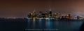 Distant Manhattan skyline illuminated above dark water under a warm night sky. Photograph by Anders Jorulf.
