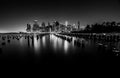 Black-and-white Manhattan skyline reflected in water behind old wooden pilings. Photograph by Anders Jorulf.