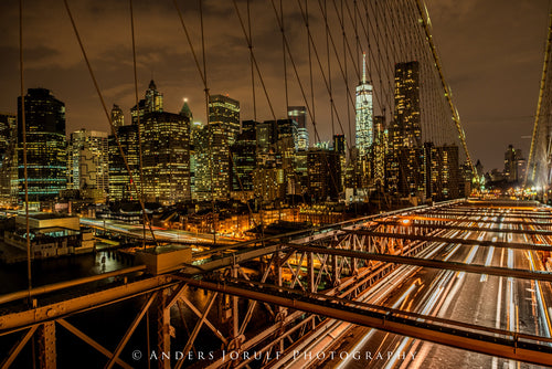 Light trails on Brooklyn Bridge beneath an illuminated Manhattan skyline. Photograph by Anders Jorulf.