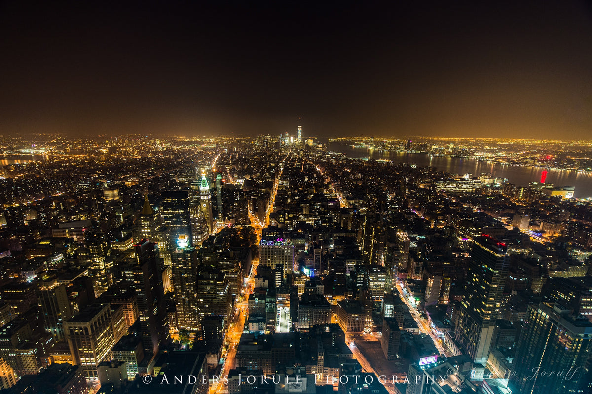An elevated view of New York at night with glowing streets and dense buildings. Photograph by Anders Jorulf.