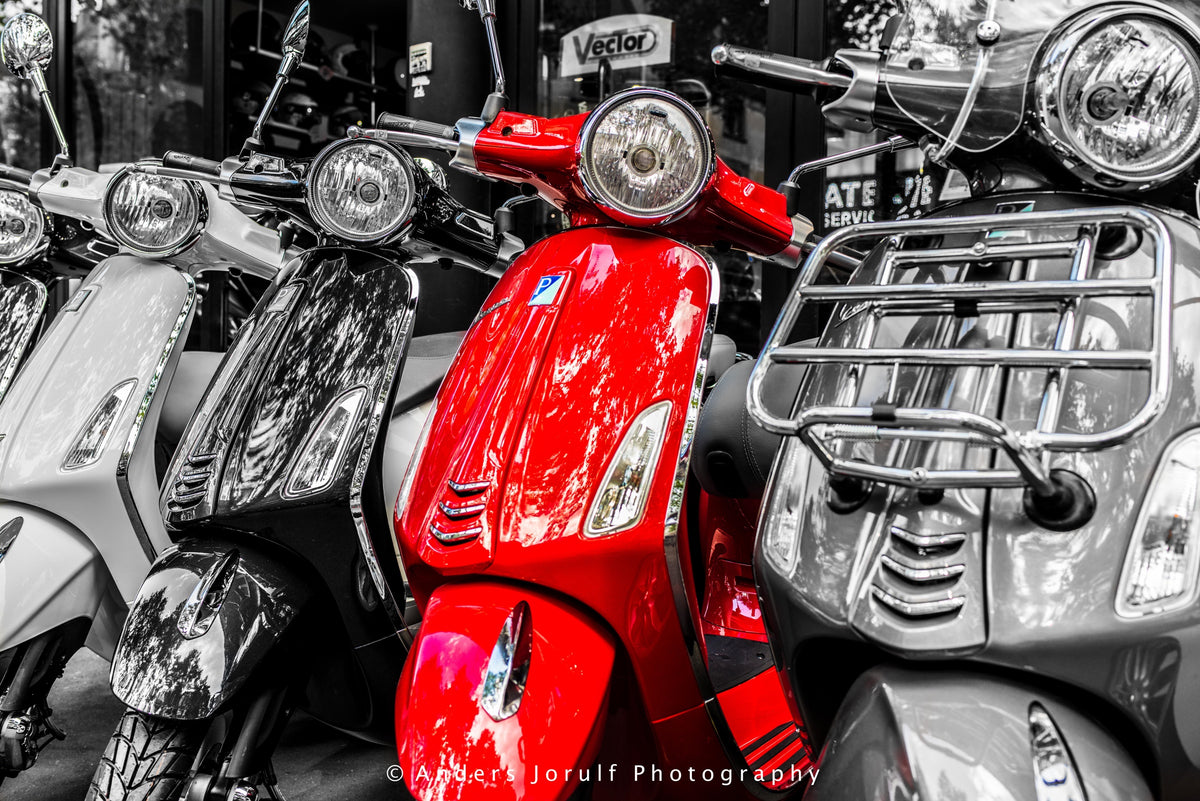 A red scooter among largely black-and-white parked scooters in Paris. Photograph by Anders Jorulf.