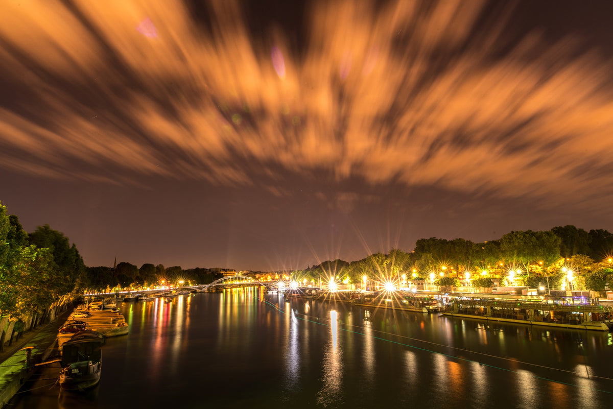 Warm lights reflected in the Seine beneath dramatically streaked clouds in Paris. Photograph by Anders Jorulf.